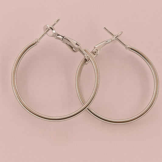 Minimalist silver-tone large hoop earrings on pink background