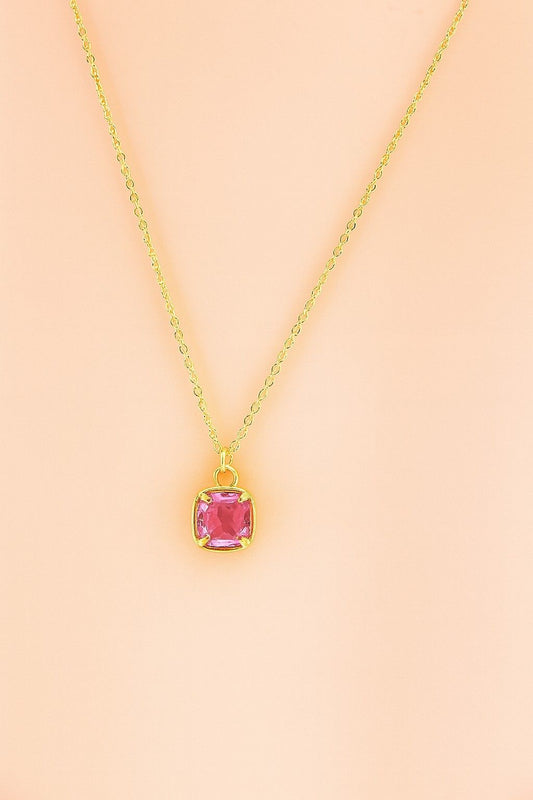 Gold-tone necklace with pink cushion cut pendant on peach background