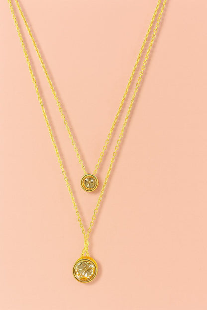 Elegant double layer gold-tone necklace with two round crystal charms on peach background