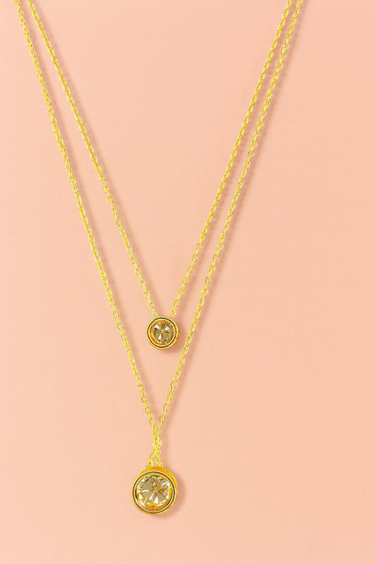 Elegant double layer gold-tone necklace with two round crystal charms on peach background