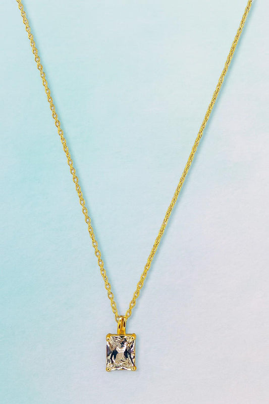 Elegant gold-tone chain necklace with square-cut crystal pendant on blue background