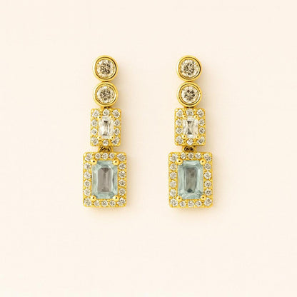 Pair of elegant gold-tone crystal drop earrings on beige background
