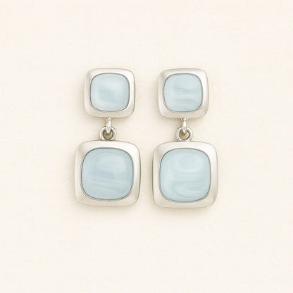 Pair of elegant silver-tone dual square drop earrings on beige background